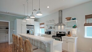 A modern kitchen with white cabinetry, a central island with bar stools, pendant lighting, and a microwave. - Coastal Escape w/ Pond Views + Pool Access | Graham’s Getaway by AvantStay (Port Aransas)