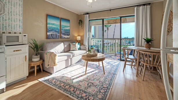 Ein Wohnzimmer mit Sofa, Couchtisch, Essbereich mit Stühlen, Deckenventilator und Blick durch eine Glastür.
