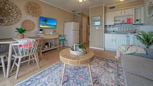 Ein Wohnzimmer mit rundem Tisch, einer Couch, einem Deckenventilator und einer Küchenzeile mit Schränken und einem Kühlschrank.