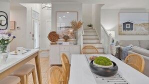 Una cocina moderna con armarios blancos, un comedor con mesa y sillas blancas, y una escalera que sube a otro nivel.