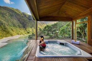 A hot tub with a wooden deck, surrounded by a wooden pergola, overlooking a river and forested hills. - Raga on the Ganges (Rishikesh)