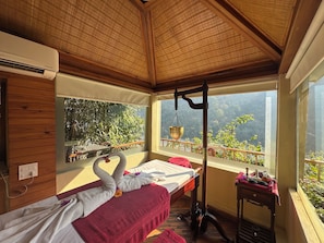 A room with a bed, a window with a view of greenery, a hanging brass bowl, and a wooden ceiling.