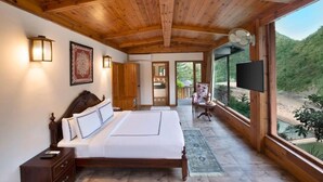 A wooden ceiling, a bed with white linens, a TV, and a view of a green landscape. - Raga on the Ganges (Rishikesh)