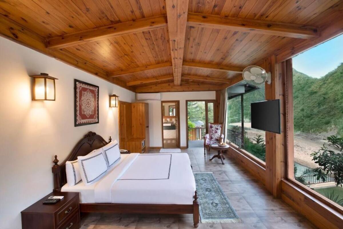 Techo de madera, cama con sábanas blancas, un televisor y vistas a un paisaje verde.