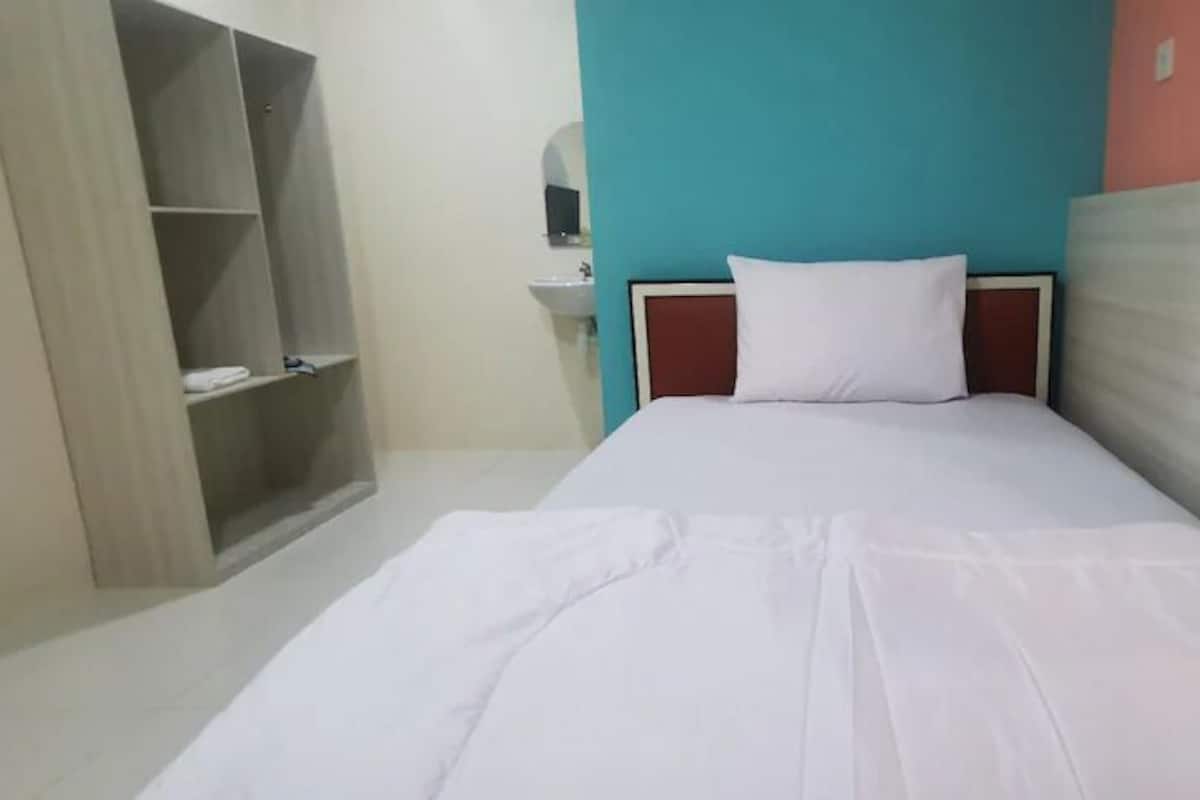Ein Einzelbett mit weißer Matratze und Kopfteil, ein Holzschrank und eine Wand in Türkis-Rot.