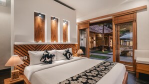 A modern hotel room with a large bed, wooden headboard, and a view of the outdoor area through glass doors. - Villa Jepun (Ubud)