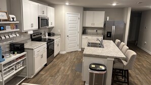 A modern kitchen with white cabinets, a stainless steel refrigerator, a microwave, and a granite countertop.