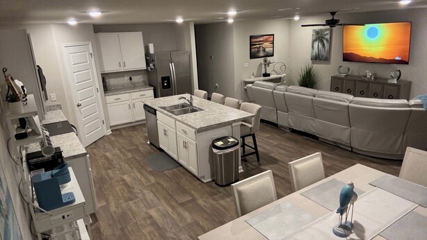 A modern kitchen with a central island, a dining area with a table and chairs, a sofa, and a TV mounted on the wall.