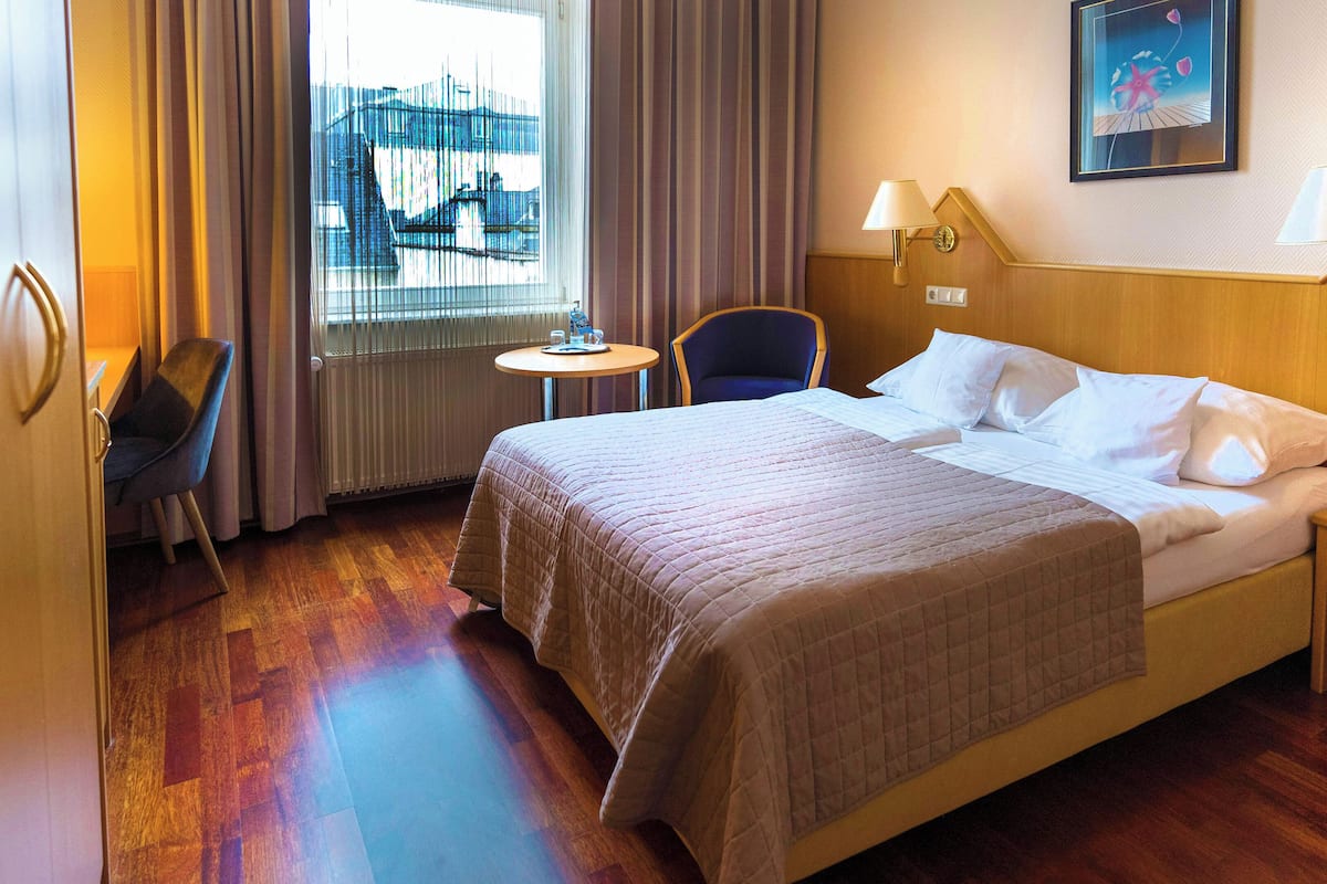 Ein Hotelzimmer mit einem großen Bett, einem Sessel, einem kleinen Tisch und einem Fenster mit Vorhängen.