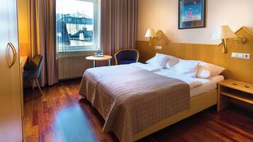Une chambre d’hôtel avec un grand lit, une chaise, une petite table et une fenêtre avec des rideaux.