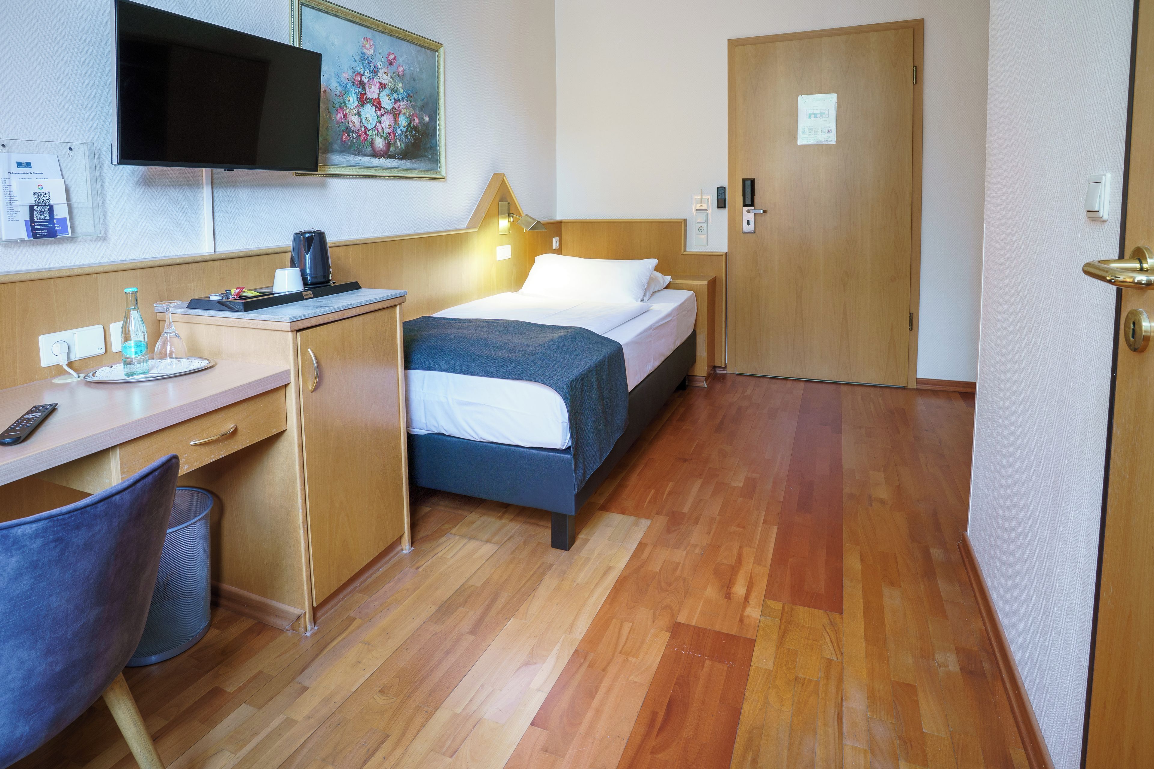 A hotel room with a bed, desk, chair, and a television mounted on the wall.