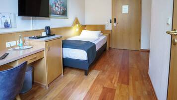 A hotel room with a bed, desk, chair, and a television mounted on the wall.