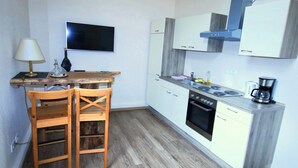 Cocina compacta con una mesa de comedor de madera, dos sillas, un televisor de pantalla plana, estufa, cafetera y armarios blancos.