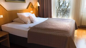 Una habitación de hotel con una cama, una mesita de noche, una lámpara y una ventana con cortinas.