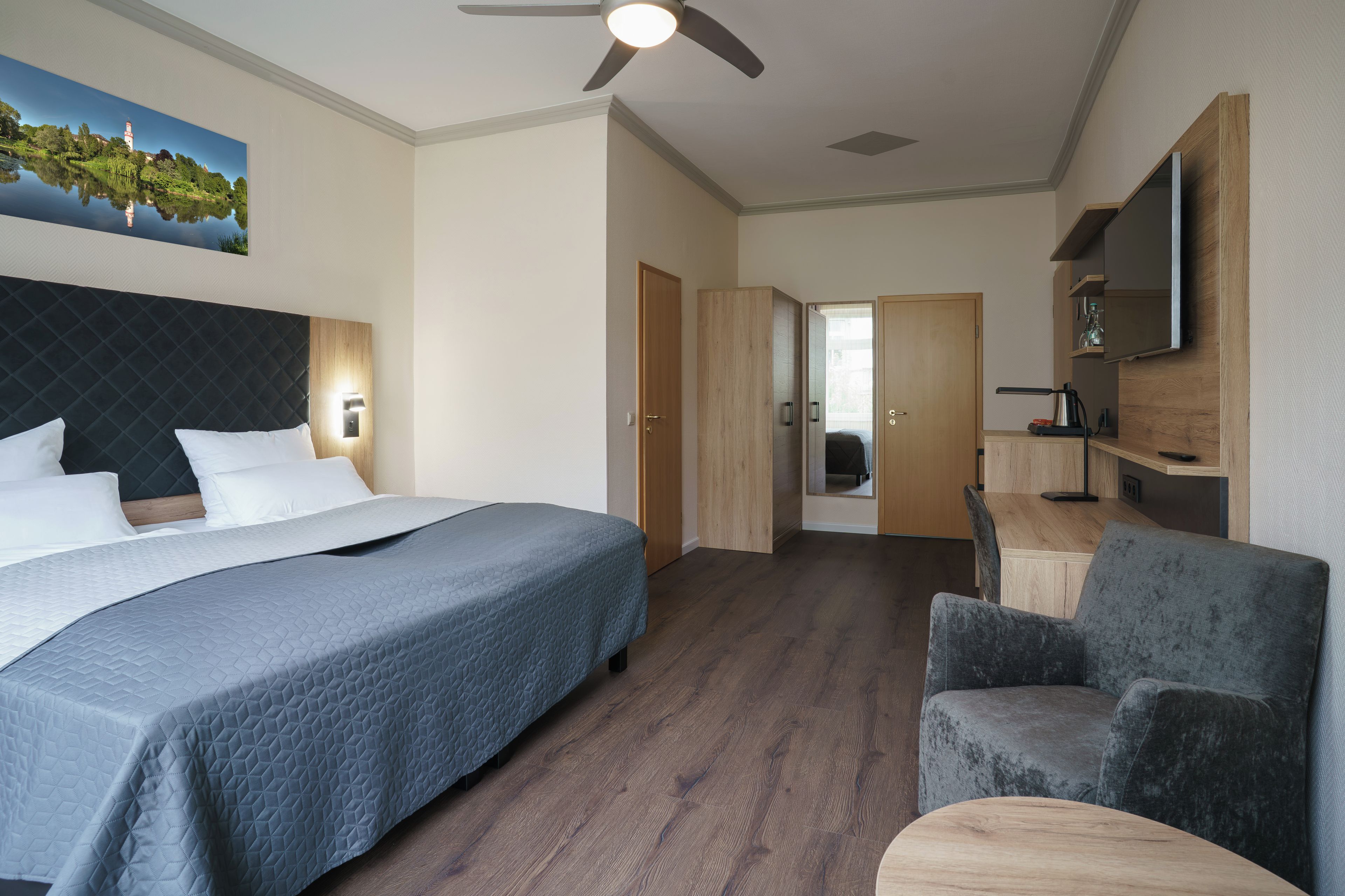 Ein Hotelzimmer mit Bett, Sessel, Schreibtisch und Fernseher.