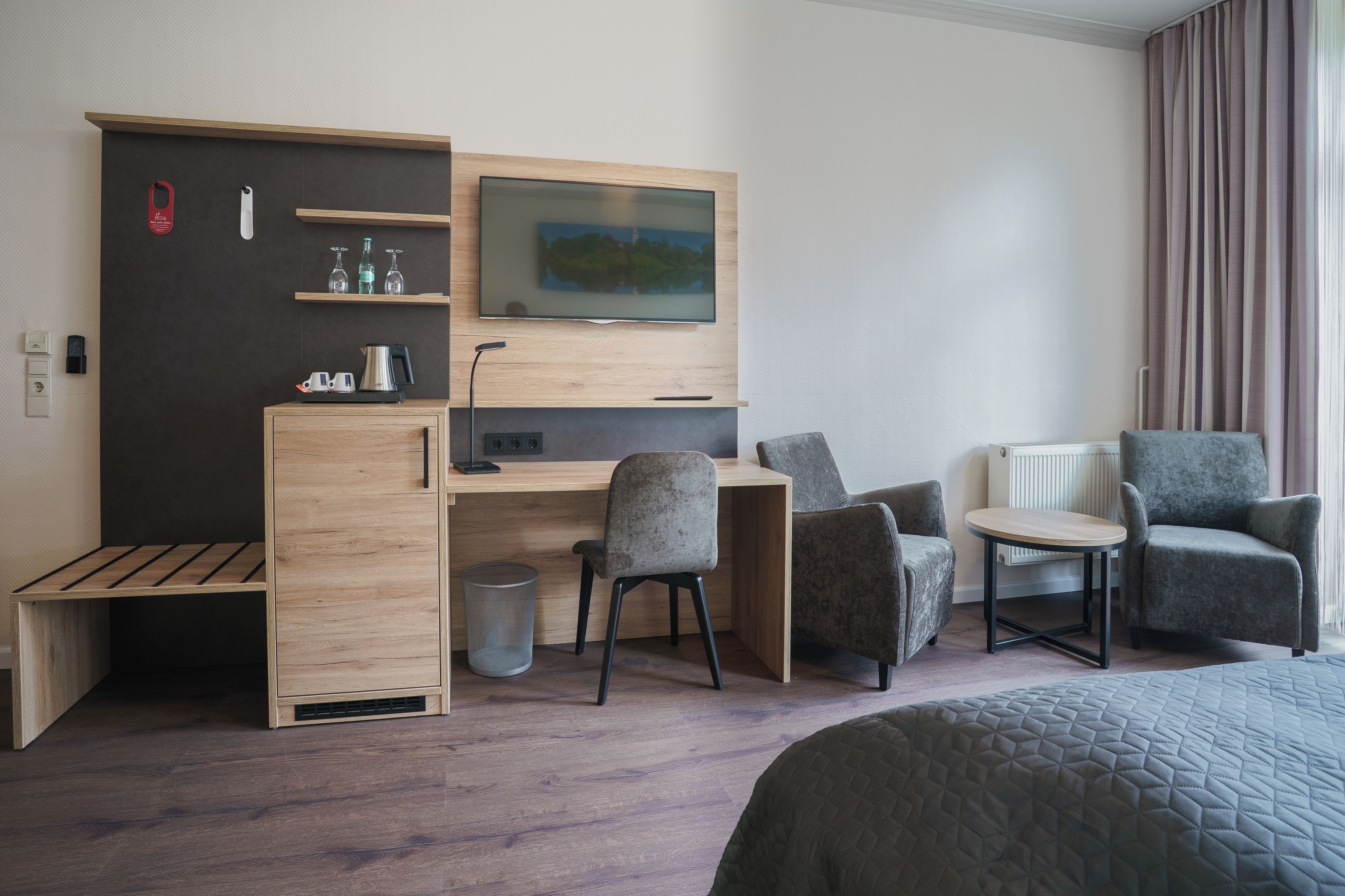 Habitación de hotel con cama, escritorio con silla, televisor y zona de estar con dos sillones.