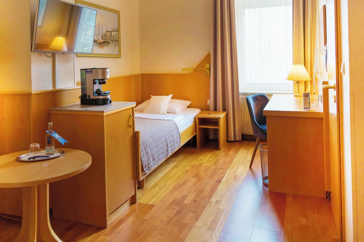 Ein Hotelzimmer mit Bett, Schreibtisch, Stuhl, einem kleinen Tisch, einer Kaffeemaschine und einem Fernseher an der Wand.