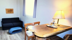 A small room with a wooden table, a lamp, a blue chair, a black sofa, and a radiator. - Komfort Hotel am Kurpark (Bad Homburg v.d. Hoehe)