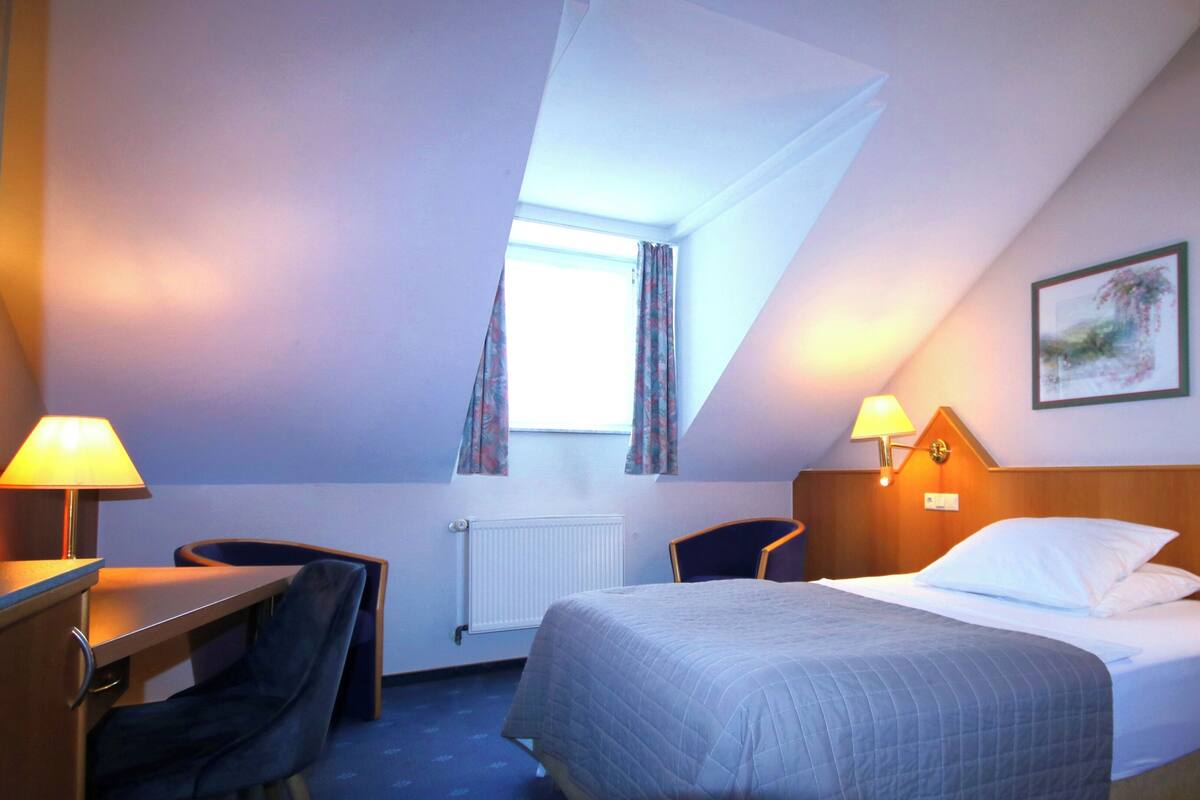 Ein Hotelzimmer mit Bett, zwei Stühlen, einem Schreibtisch und einem Fenster mit Vorhängen.