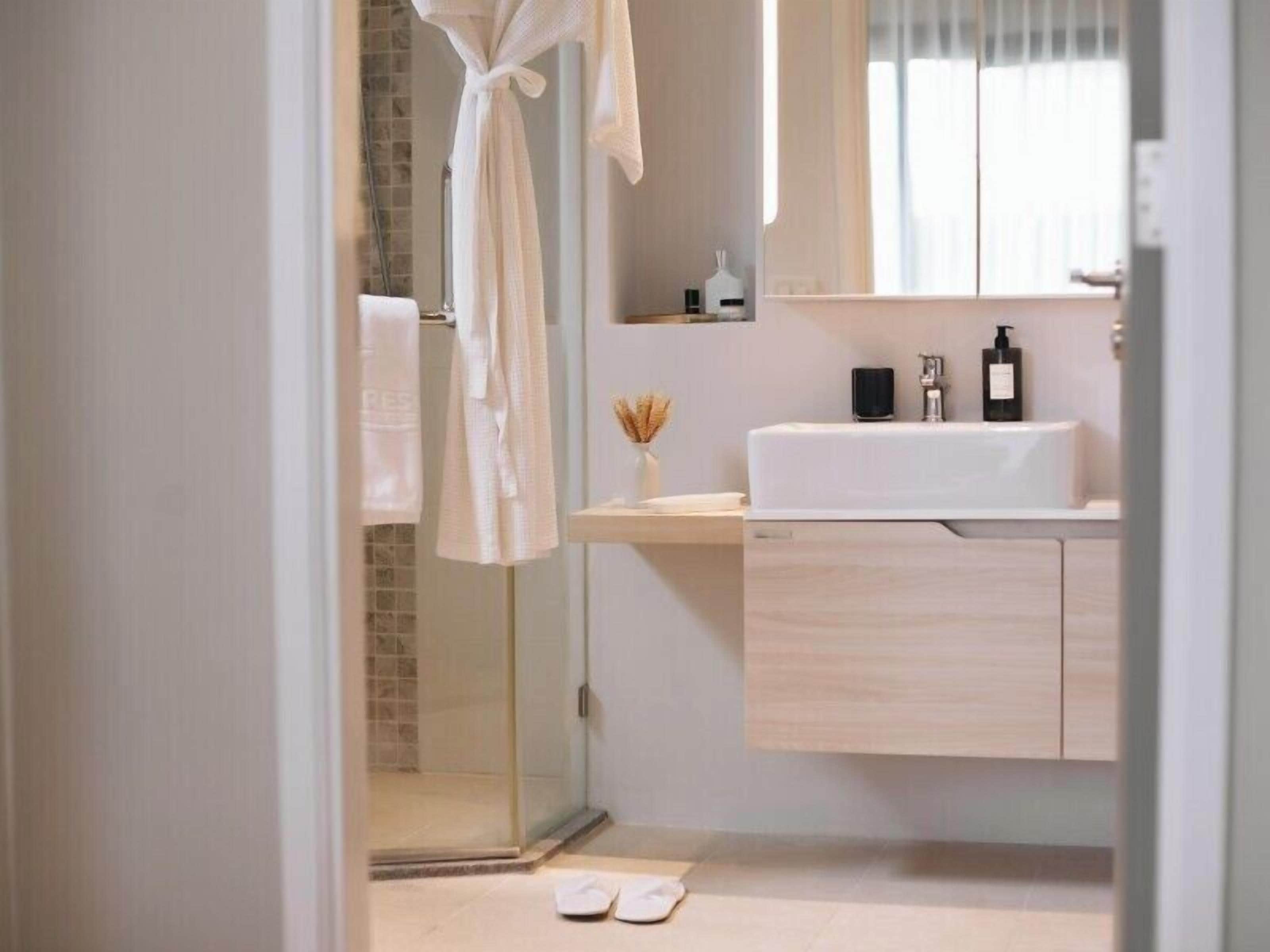 Une salle de bain moderne avec une douche à l’italienne en verre, un lavabo blanc et un meuble-lavabo en bois.