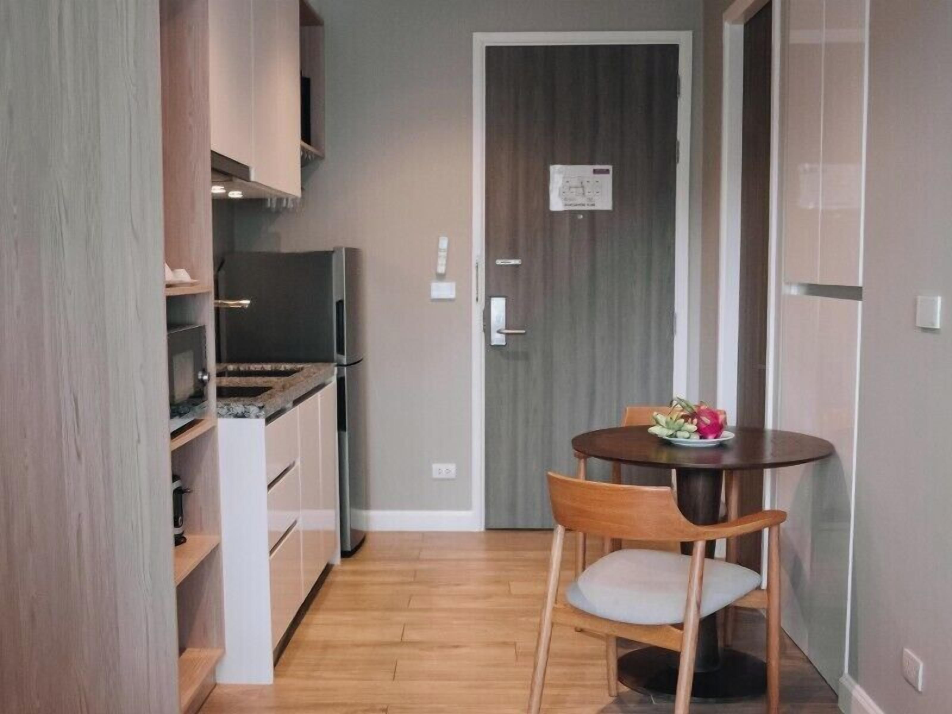A compact kitchen with a dining area, including a refrigerator, microwave, and wooden cabinets.