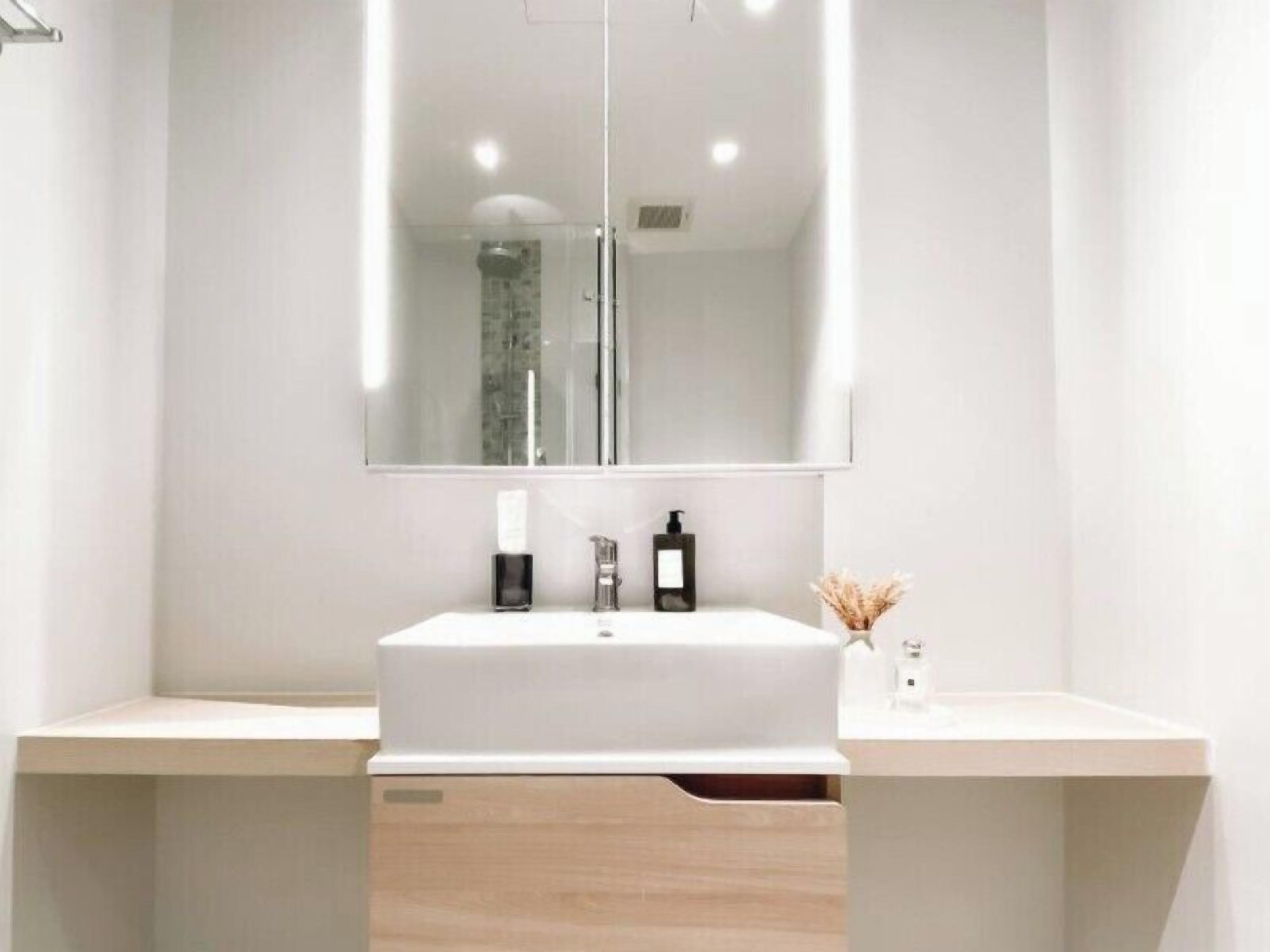 A modern bathroom with a large mirror, a white sink, and a wooden cabinet below.