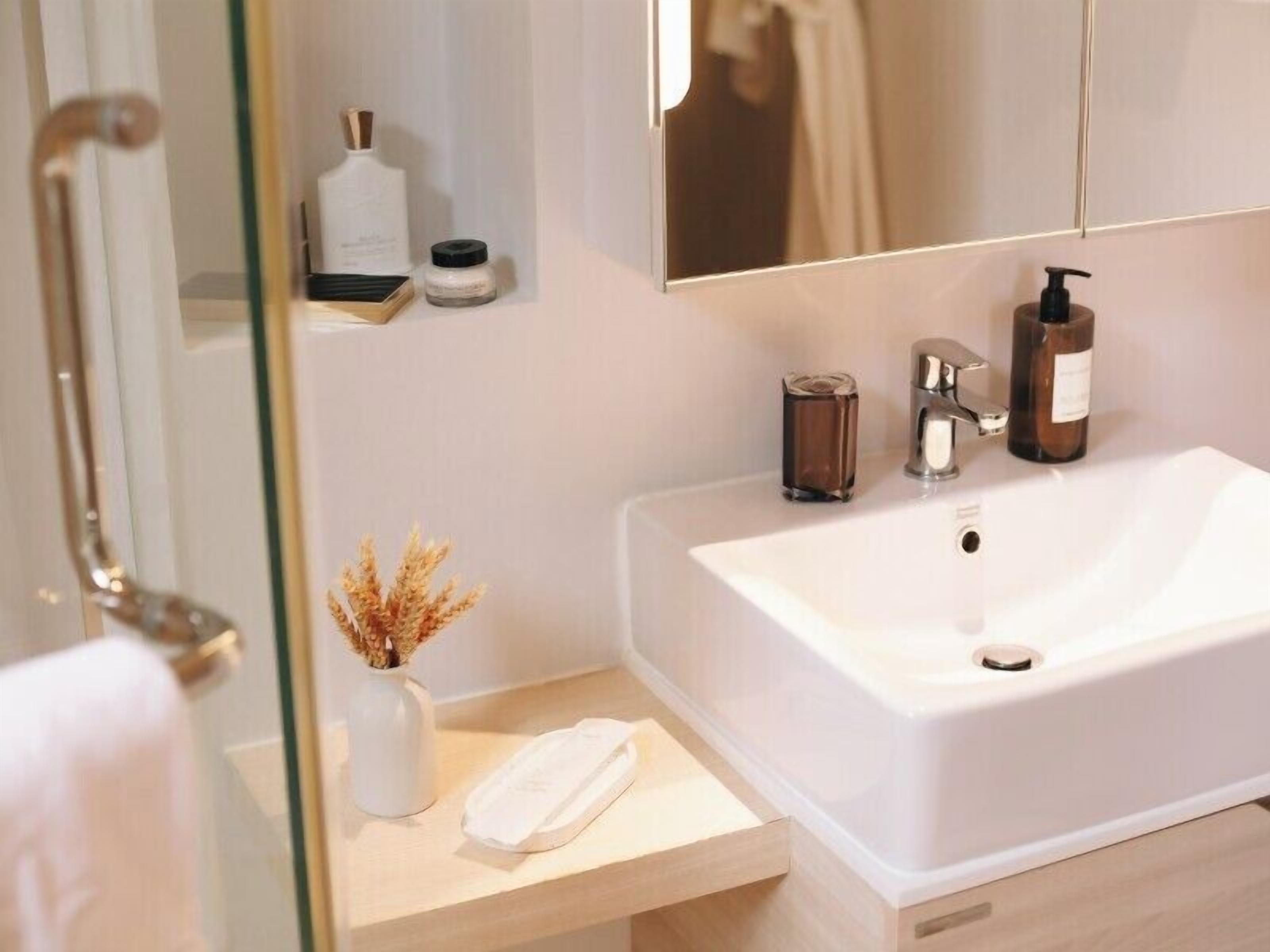 Une salle de bain avec un lavabo blanc, un miroir, une serviette et un petit vase contenant des fleurs séchées.