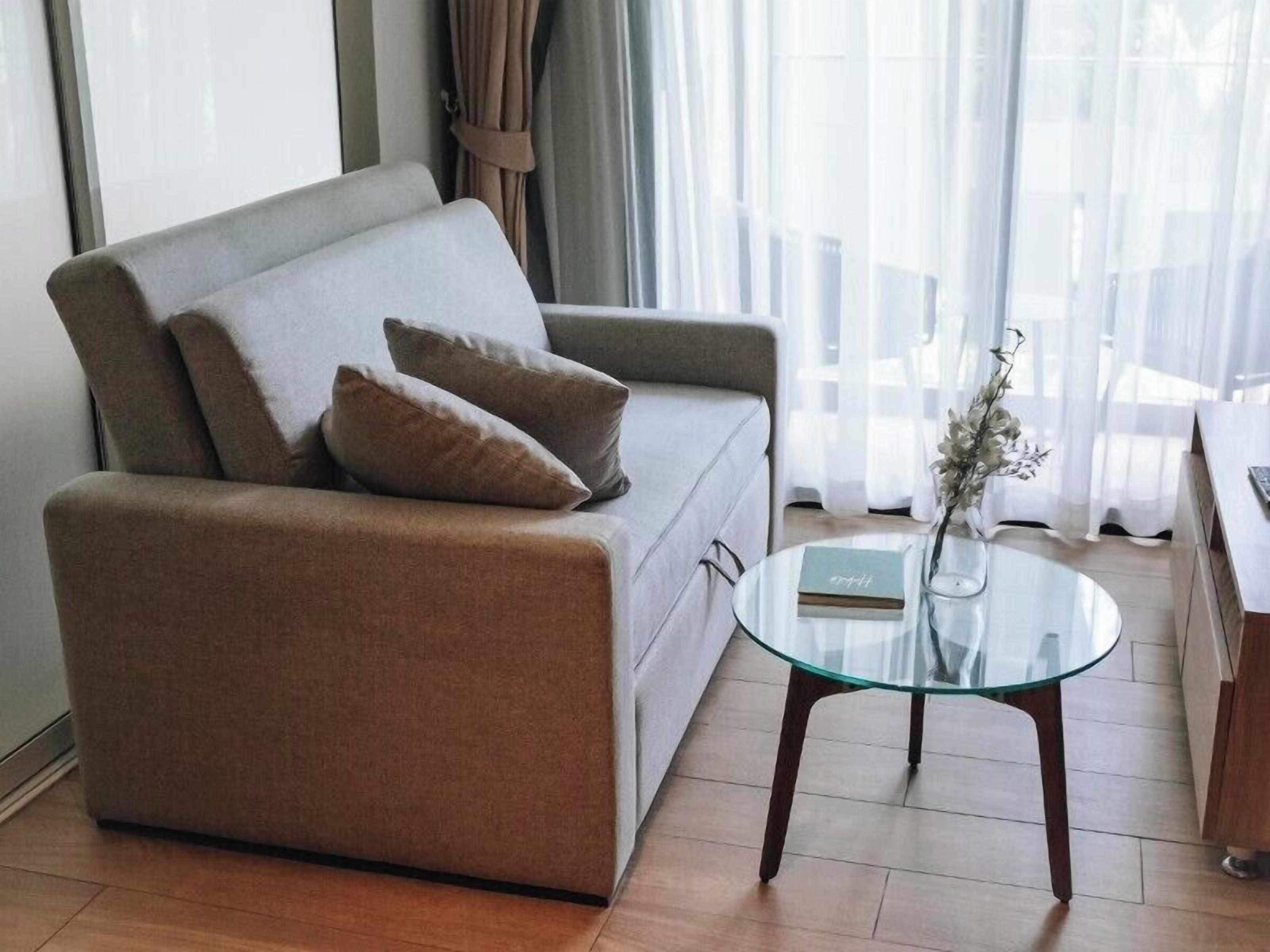 A modern living room with a grey sofa, two cushions, a glass coffee table, and a book.
