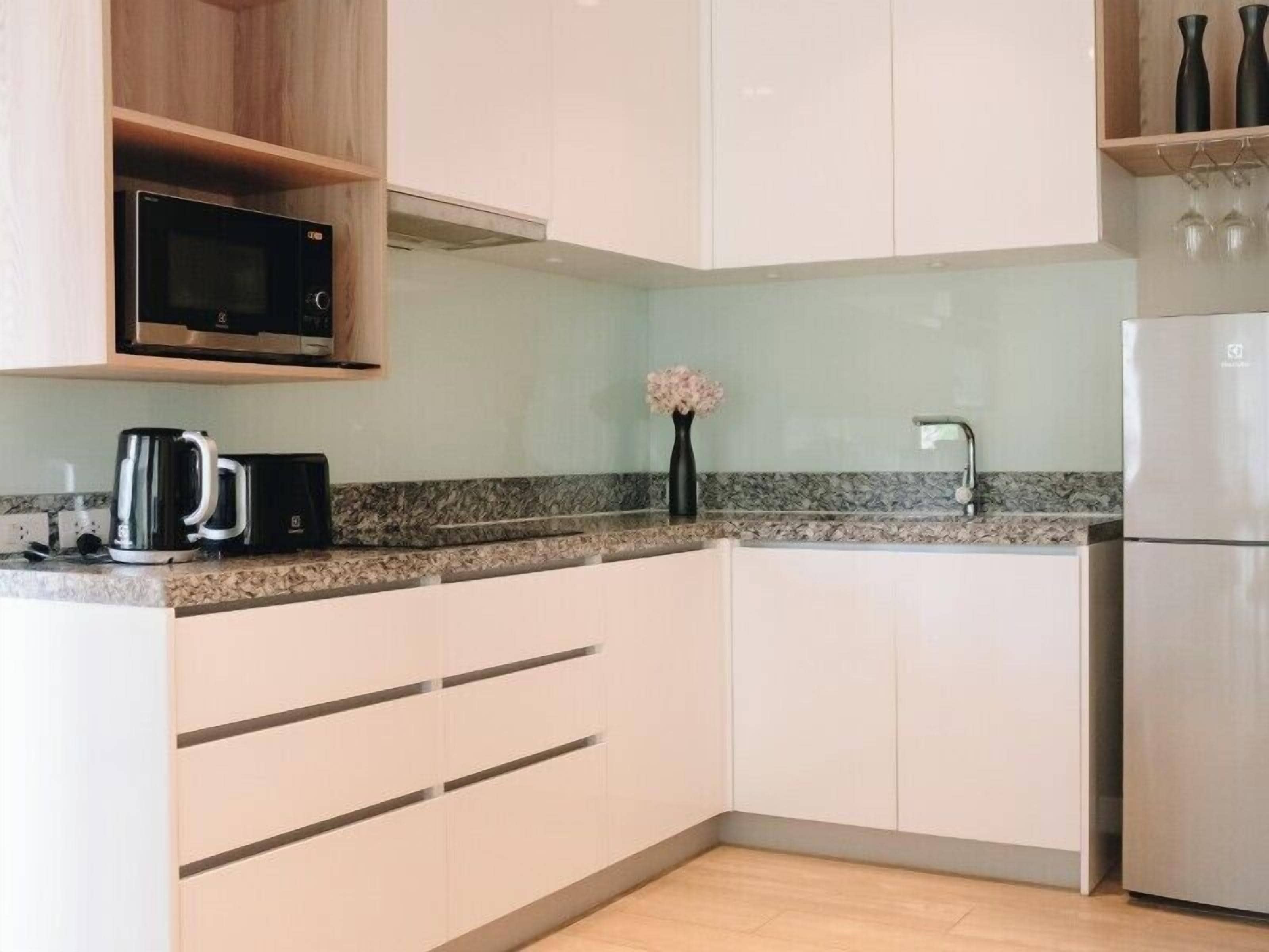 A modern kitchen with white cabinets, a stainless steel refrigerator, a microwave, and a coffee maker.