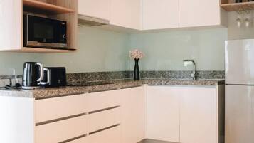 Una cocina moderna con armarios blancos, un refrigerador de acero inoxidable, un microondas y una cafetera.