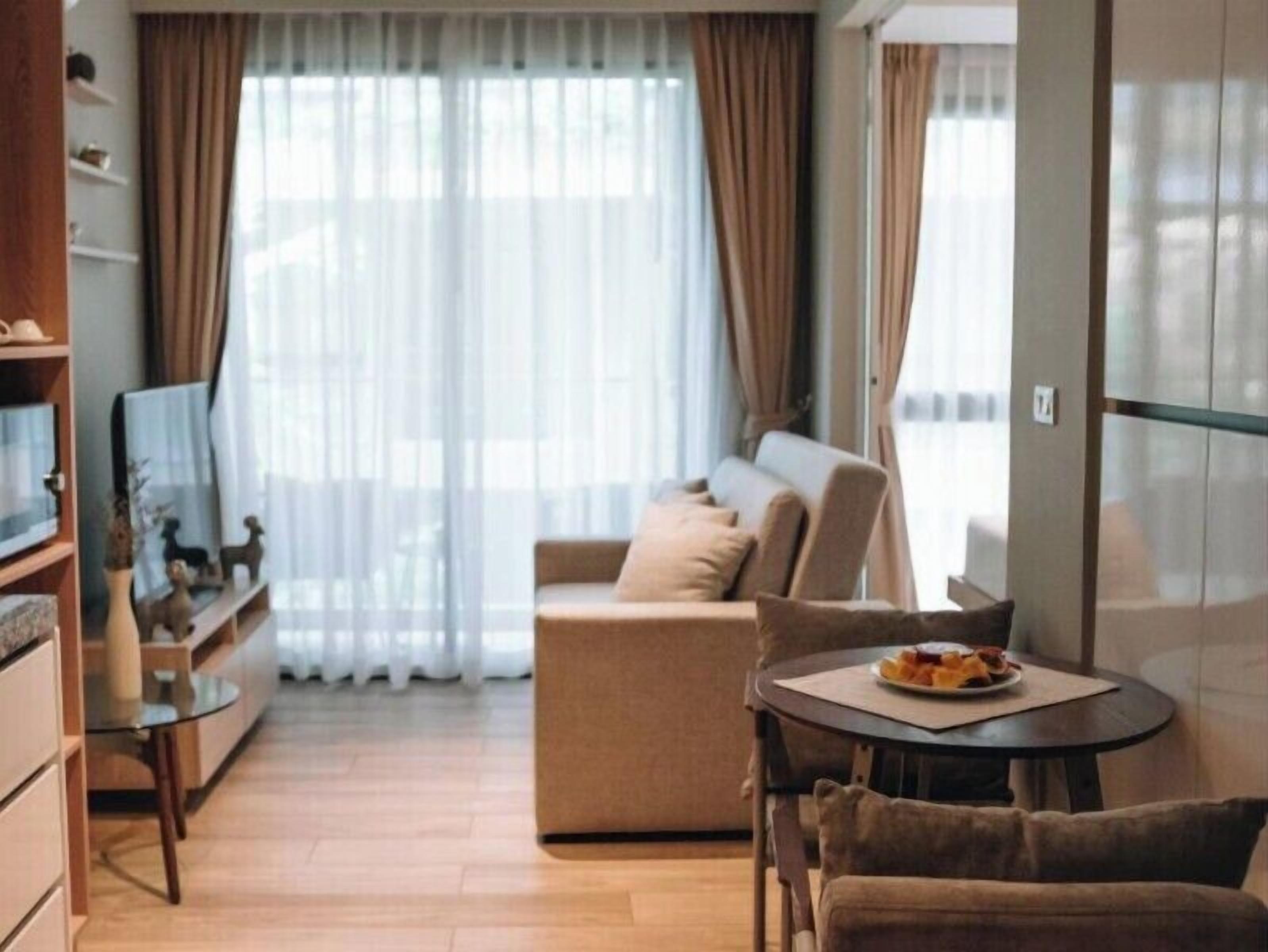 Un salon moderne avec un canapé, une table à manger et des chaises, ainsi qu’un téléviseur posé sur un meuble.
