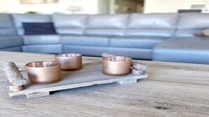 A wooden tray with three copper-colored cups and a decorative item on a table in a living room with a grey sofa. - Studio in Belgium with Sea View & Balcony (MIDDELKERKE)
