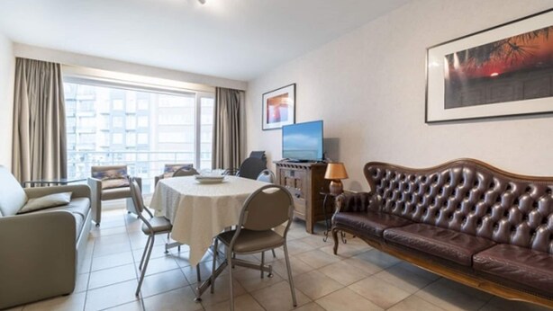 Une chambre d’hôtel comprenant un coin repas, un canapé, une télévision et une grande fenêtre avec des rideaux.