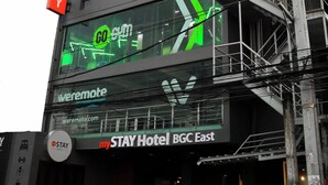 A hotel with a large digital sign advertising a gym, a remote control sign, and the name "STAY Hotel BGC East". - mySTAY BGC East (Makati)