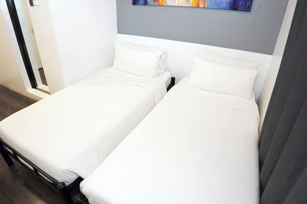 Two single beds with white bedding in a room with a grey accent wall and a colorful abstract painting above the beds.