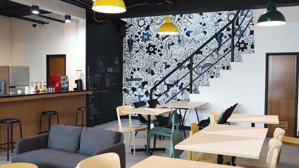 A modern cafe with a black and white mural, wooden tables, and a grey sofa. - mySTAY BGC East (Makati)