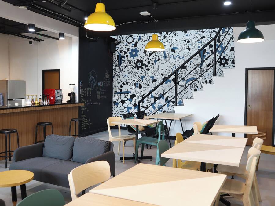 Un caffè moderno con un murale bianco e nero, tavoli in legno e un divano grigio.