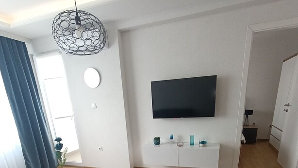 A modern living room with a flat-screen TV, a round coffee table, and a dining area with a wooden table and chairs.
