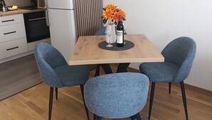 A modern kitchen with white cabinets, a refrigerator, and a sink. There is a dining table with two chairs and a vase with flowers.
