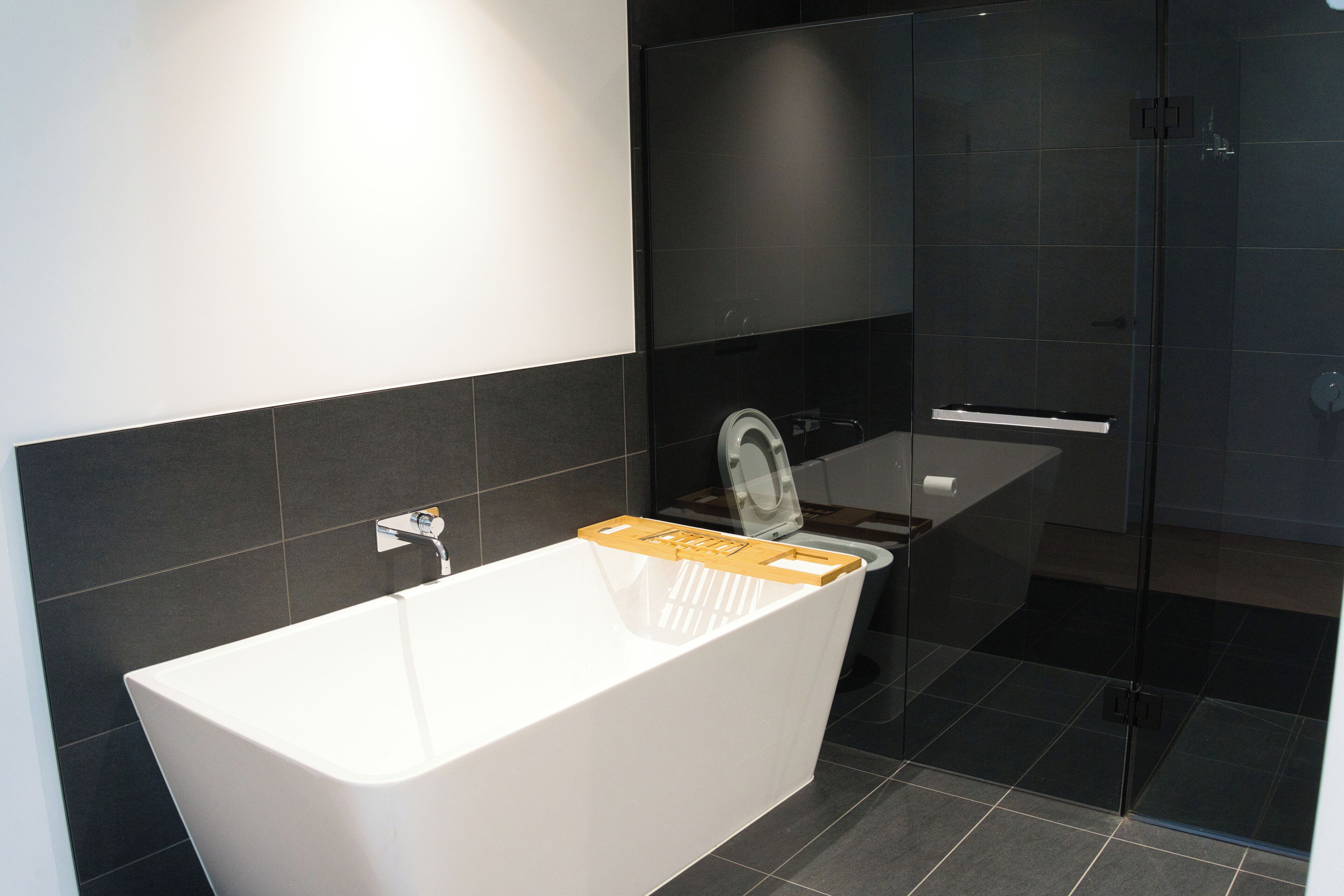 Ein modernes Badezimmer mit freistehender Badewanne, einer Duschkabine aus Glas und dunkel gefliesten Wänden.