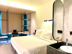A modern hotel room with a large bed, a desk with a laptop, a chair, a shelf with toiletries, and a large mirror. - ATOOI Hotel Alam Sutera (South Tangerang)