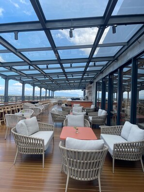 A rooftop bar with wicker furniture, glass railings, and a view of the city skyline. - ATOOI Hotel Alam Sutera (South Tangerang)