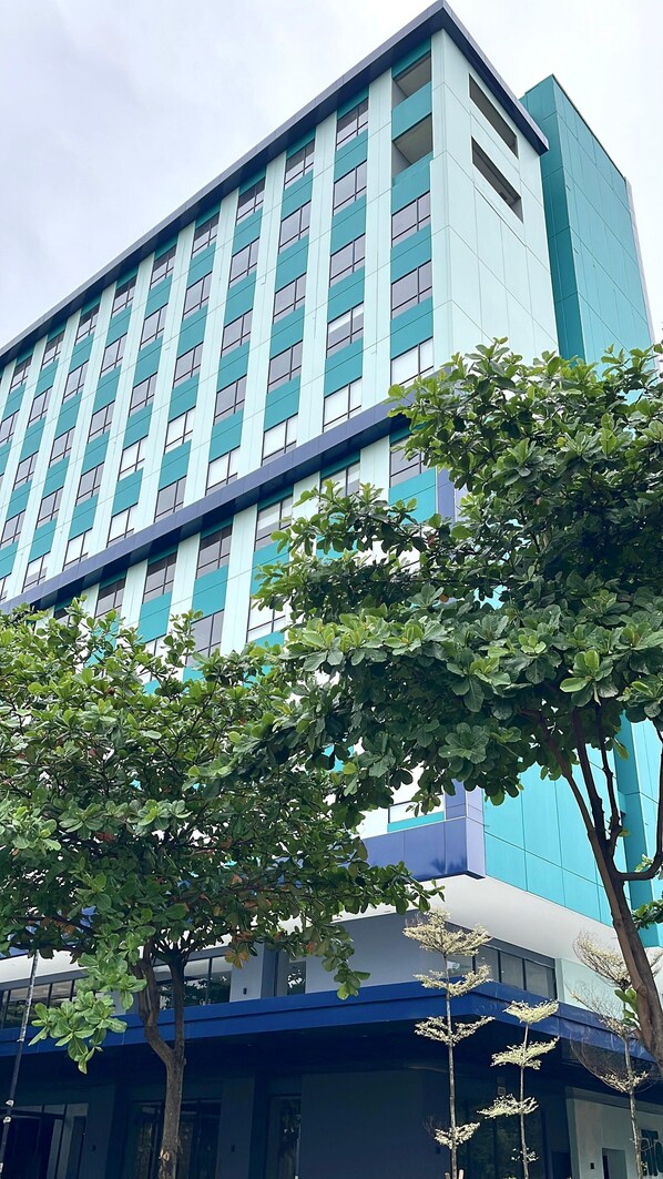A modern building with a blue and white facade, large windows, and a tree in the foreground. - ATOOI Hotel Alam Sutera (South Tangerang)