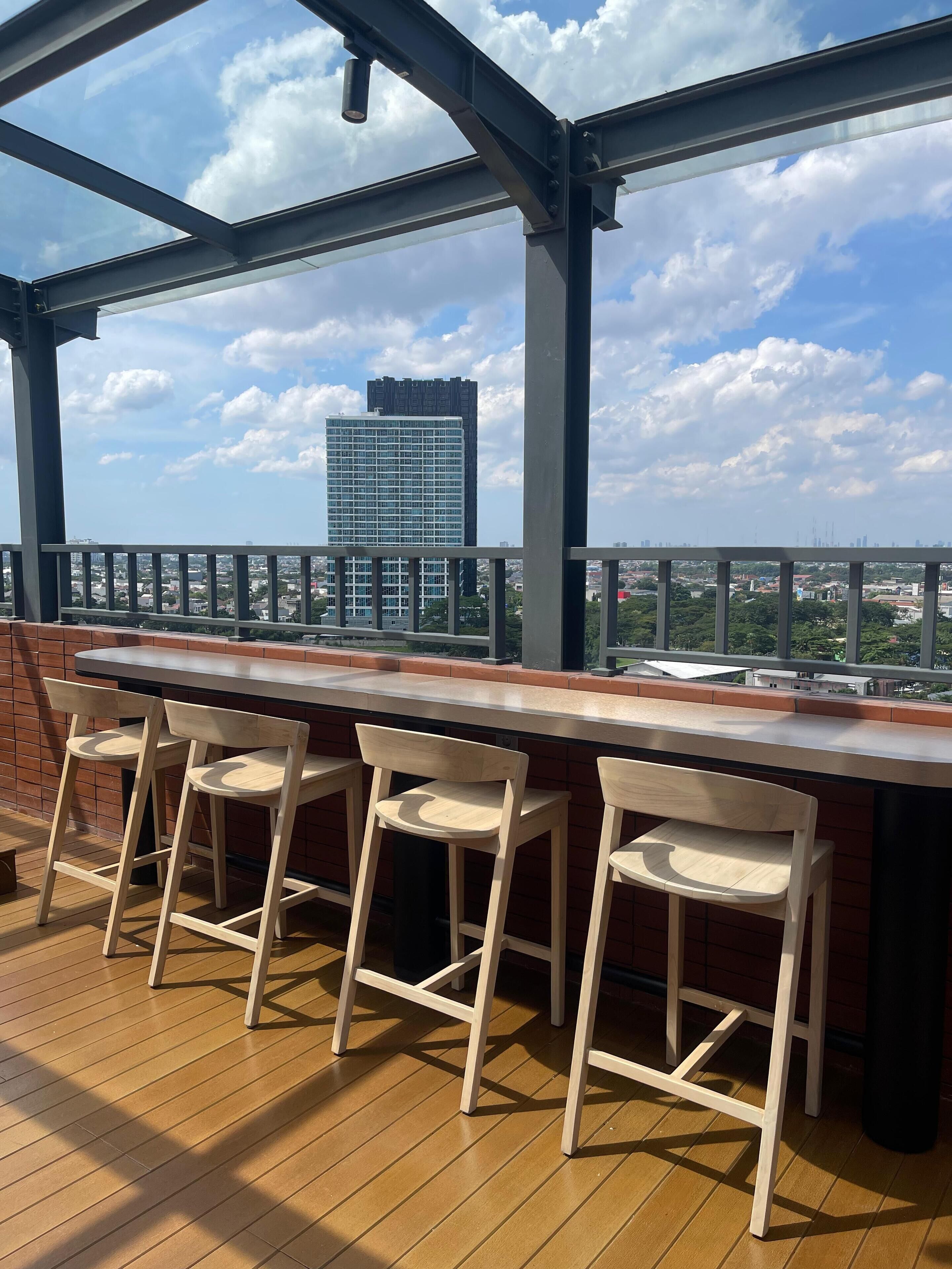 Ein überdachter Außenbereich mit Bar, Holzsesseln und Blick auf die Stadtlandschaft.