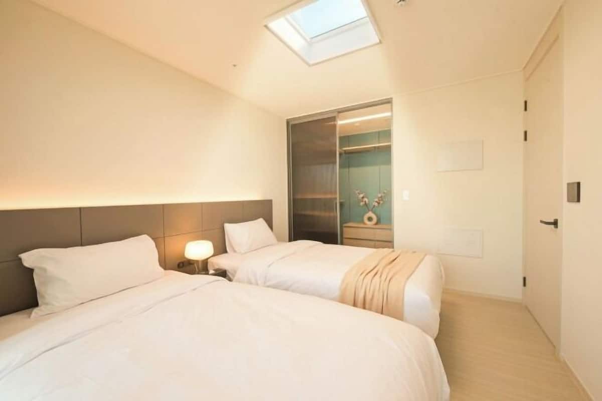 A hotel room with two beds, a skylight, a walk-in closet, and a bedside table with a lamp.