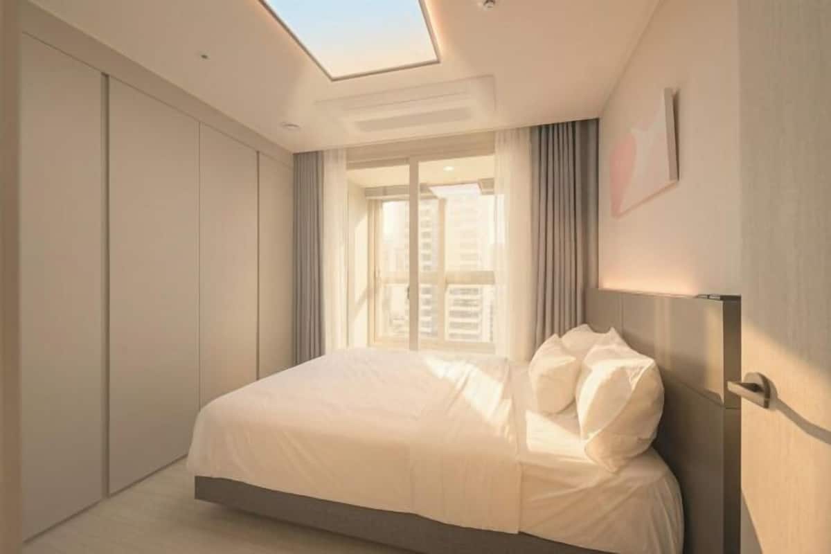 A bedroom with a skylight, a bed, a wardrobe, and a view of buildings outside.