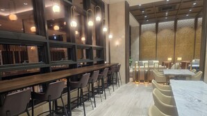 A modern bar area with high stools and a long counter, a seating area with tables and chairs, and a decorative wall with perforated panels. - SOTA SUITE Busan Seomyeon (Busan)