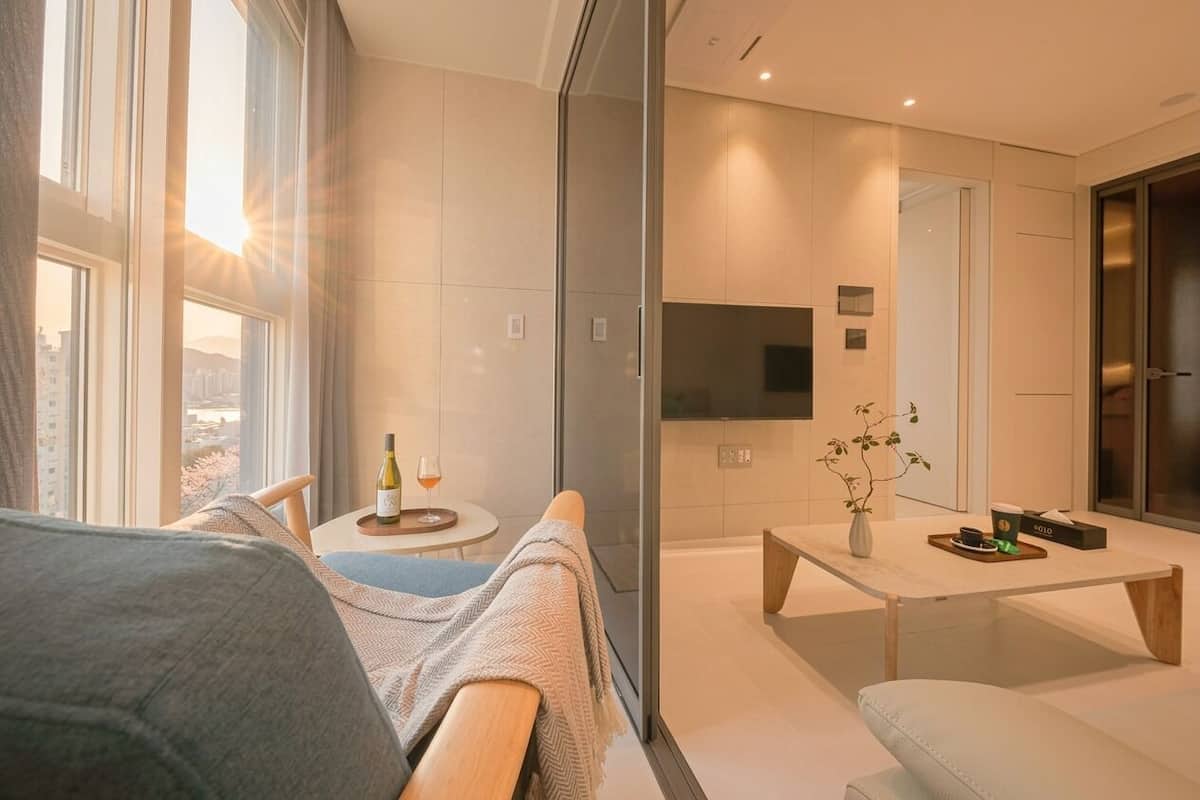 A modern hotel room with a sofa, a coffee table, a TV, and a view of the city.