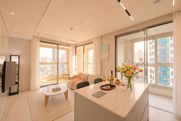 A modern living room with a sofa, coffee table, and a dining area with a glass top table. - SOTA SUITE Busan Seomyeon (Busan)