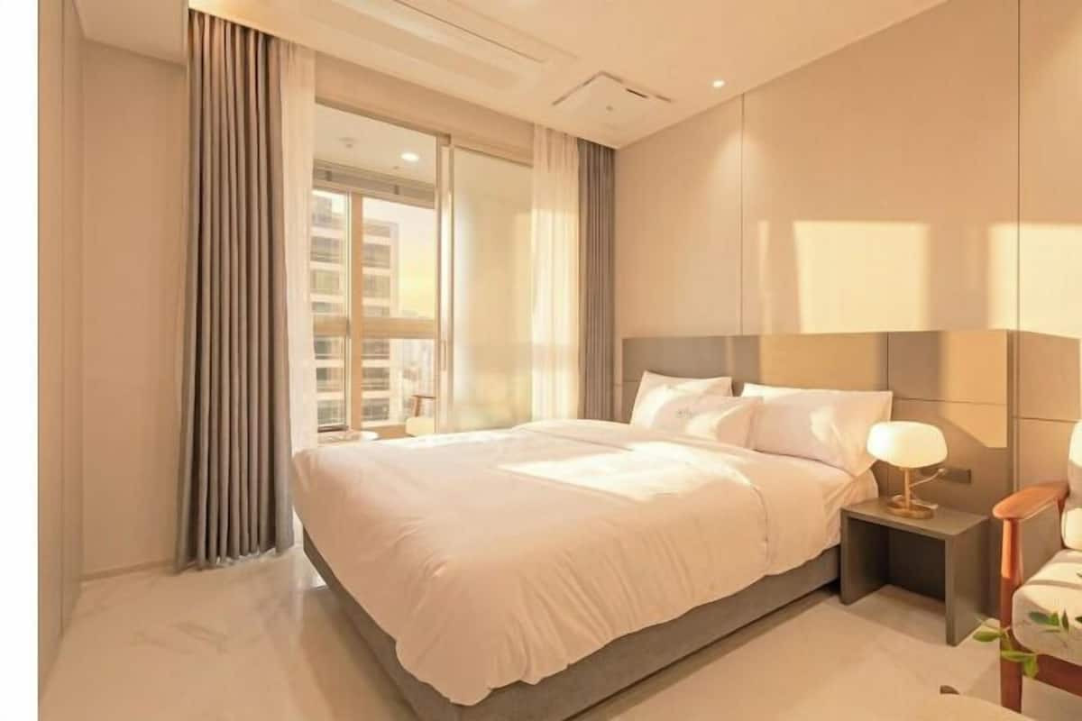 A modern hotel room with a large bed, a nightstand with a lamp, a view of the city through the window, and a clean, minimalist design.